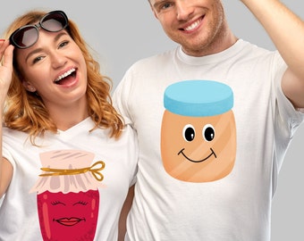 May include: A couple wearing white t-shirts with a cartoon jar of jam and a cartoon jar of peanut butter on them. The jar of jam has a red lid and a smiling face with red lips. The jar of peanut butter has a blue lid and a smiling face with brown eyes.