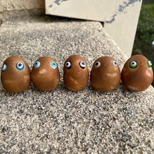 May include: Six small brown potato-shaped figurines with googly eyes. The eyes are blue, black, and green.