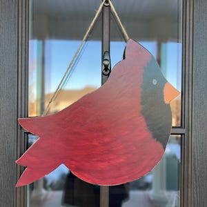 May include: A red cardinal bird wooden cutout with black accents, hanging from a string on a door.