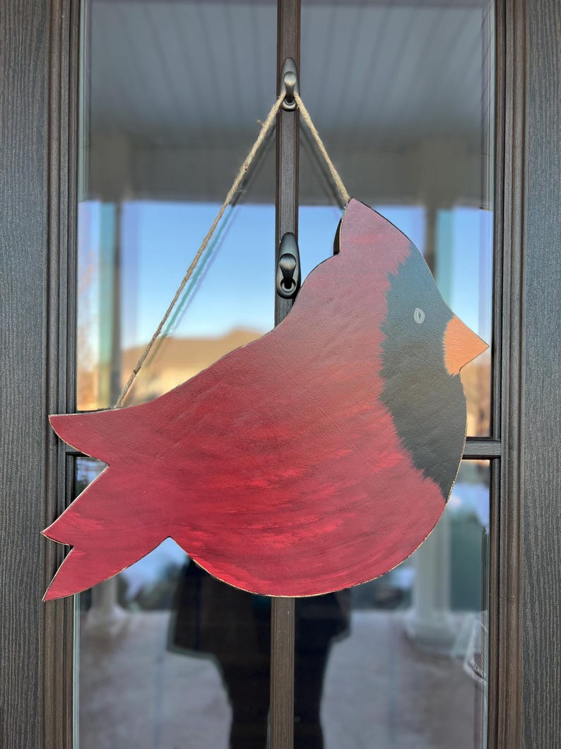 May include: A red cardinal bird wooden cutout with black accents, hanging from a string on a door.