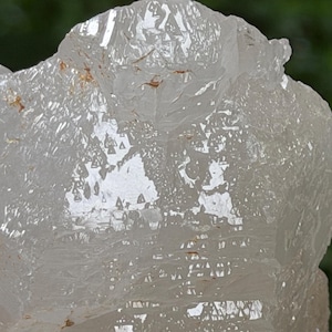 May include: A clear, translucent quartz crystal specimen featuring a jagged, multi-faceted surface with sharp, angular edges and small, triangular geometric patterns etched into the crystalline structure, showing internal fractures and light reflections.