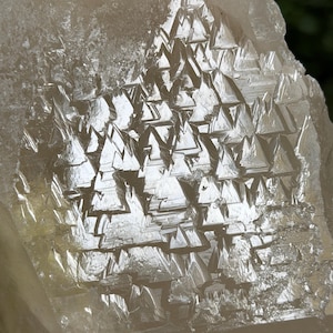 May include: Close-up of a raw mineral specimen. The stone is a pale, translucent colour with a crystalline structure. The surface features a pattern of small, geometric shapes, creating a textured appearance. The overall aesthetic is earthy and organic.