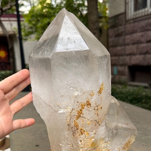 May include: A large, clear quartz crystal with a pointed top, mounted on a wooden base. The crystal has natural inclusions and a slightly yellow hue. The base is a light brown colour. The crystal is a decorative item.
