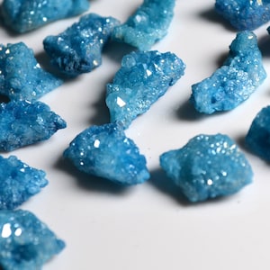 Può includere: Una collezione di grappoli di cristalli blu con bagliori iridescenti. I cristalli sono di varie dimensioni e forme, e hanno una texture ruvida e naturale.