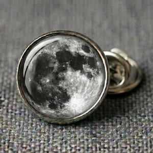 Full moon lapel pin silver tone brass with photorealistic moon surface craters epoxy dome, displayed on grey fabric, astronomy space celestial gift.