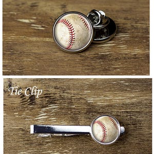 May include: A baseball-themed lapel pin and tie clip. The pin is round with a baseball design, featuring red stitching on a beige background. The tie clip has a similar baseball design. The text "Lapel Pin" and "Tie Clip" are visible.