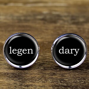 May include: A pair of cufflinks with black backgrounds and silver rims. The left cufflink says "legen" and the right cufflink says "dary".