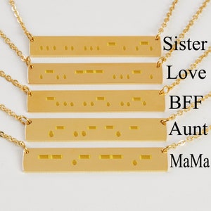May include: Five gold necklaces with bar pendants engraved with words in braille. The words are "Sister", "Love", "BFF", "Aunt", and "MaMa".