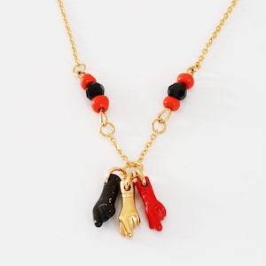 May include: Gold chain necklace with red and black beads and three gold charms shaped like hands. Two of the charms are black and one is gold.