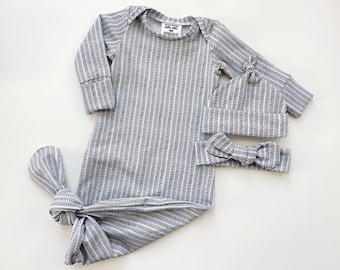 May include: A black and white chevron patterned baby gown with matching headband and knotted bottom. The gown has long sleeves and a round neckline. The headband is tied in a bow.