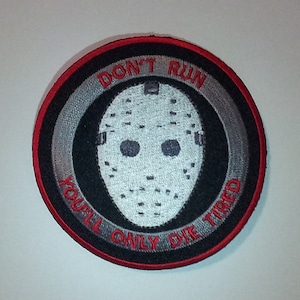 May include: A black and white embroidered patch with a hockey mask and the text "Don't Run You'll Only Die Tired". The patch has a red border and a silver ring around the mask.