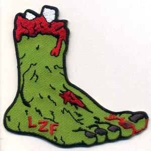 May include: Green zombie foot with red blood dripping down the leg. The foot has three toes and the letters "LZf" are embroidered on the bottom of the foot.