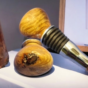 May include: Two wooden bottle stoppers, one with a silver and gold metal top. The stoppers are on a white surface.
