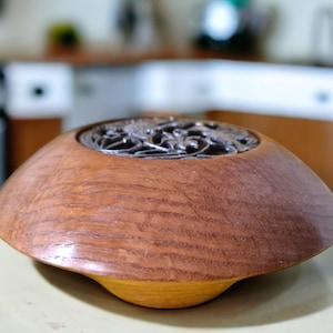 Pode incluir: Uma tigela de madeira com um inserto de metal decorativo. A tigela é de cor castanho claro e tem um acabamento liso e polido.