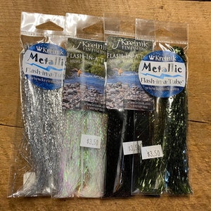 Puede incluir: Cuatro paquetes de material de atado de moscas Kreinik Metallic Flash-in-a-Tube. Los colores son plata, perla, negro y verde. Cada paquete está etiquetado con el logotipo de Kreinik y el nombre del producto. El precio es de 3,50 € por paquete.