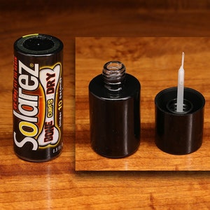 Puede incluir: Una botella negra de resina UV Solarez con una etiqueta blanca que dice "Solarez" y "Bone Cures Dry Under 10 Seconds". La botella está al lado de una botella negra con una tapa de vidrio transparente y un pincel aplicador blanco.