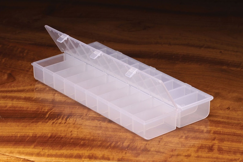 K&ouml;nnte beinhalten: Eine transparente Plastik-Aufbewahrungsbox mit einem Scharnierdeckel und mehreren F&auml;chern. Die Box ist ge&ouml;ffnet und der Deckel ist hochgeklappt.