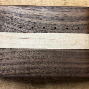 May include: A wooden box with a light wood inlay and a brass nail. The box has a series of holes drilled into the top.
