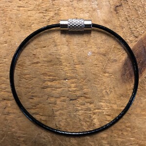 Könnte beinhalten: Ein schwarzer Leder-Schlüsselanhänger mit einem silbernen Metallverschluss.