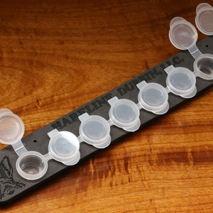 May include: A black paint palette with the text "HARRELLIN DURBIN, INC."  The palette has eight small, clear paint pots with lids.  The lids are hinged and open to reveal the paint pots.
