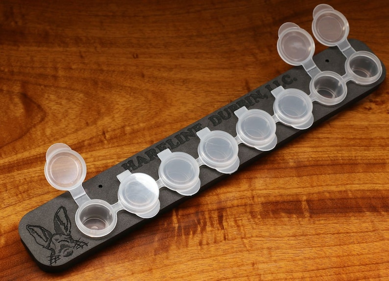 May include: A black paint palette with the text "HARRELLIN DURBIN, INC."  The palette has eight small, clear paint pots with lids.  The lids are hinged and open to reveal the paint pots.