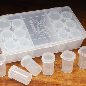 May include: A clear plastic box with 18 small clear plastic containers. The box is labeled "Hareline Dubbin, LLC. Fly Tyers Conceal Carry Stash Box".