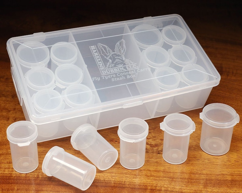 May include: A clear plastic box with 18 small clear plastic containers. The box is labeled "Hareline Dubbin, LLC. Fly Tyers Conceal Carry Stash Box".