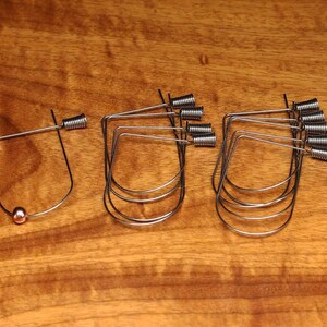May include: A set of ten silver wire hoops with a small copper bead on one hoop. The hoops are all the same size and shape, and they are arranged in a row on a wooden surface.