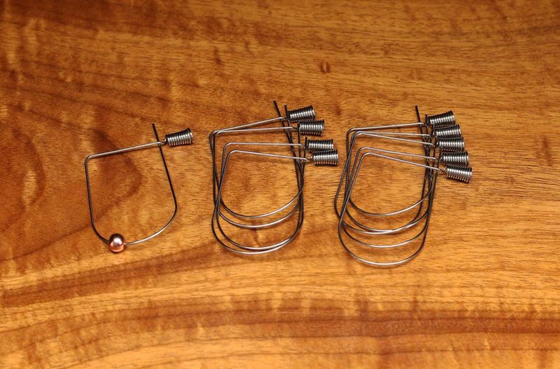 May include: A set of ten silver wire hoops with a small copper bead on one hoop. The hoops are all the same size and shape, and they are arranged in a row on a wooden surface.