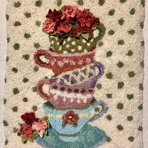 May include: A decorative, textured pillow featuring a stack of four teacups in shades of red, purple, pink, and blue. Each cup is adorned with intricate patterns and topped with fabric flowers. The background is off-white with green polka dots.