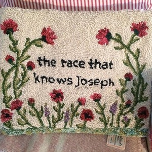 K&ouml;nnte beinhalten: Ein rechteckiges, cremefarbenes, getuftetes Kissen mit dem Text "the race that knows Joseph" in Schwarz. Es zeigt rote Blumen und gr&uuml;ne Stiele mit einem Rand aus gr&uuml;nen und lila Blumen.
