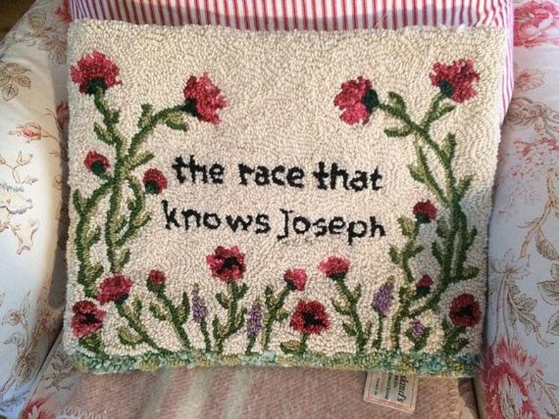 K&ouml;nnte beinhalten: Ein rechteckiges, cremefarbenes, getuftetes Kissen mit dem Text "the race that knows Joseph" in Schwarz. Es zeigt rote Blumen und gr&uuml;ne Stiele mit einem Rand aus gr&uuml;nen und lila Blumen.