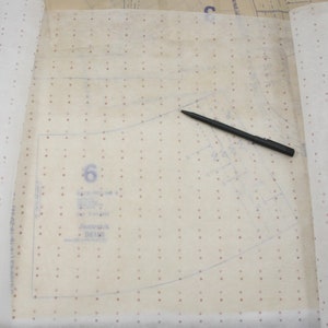 K&ouml;nnte beinhalten: Ein Schnittmuster mit der sichtbaren Zahl 6, zusammen mit der Marke "Butterick" und der Schnittnummer B6198. Ein schwarzer Stift liegt auf dem Muster. Das Muster befindet sich auf einem hellen, gepunkteten Papier.