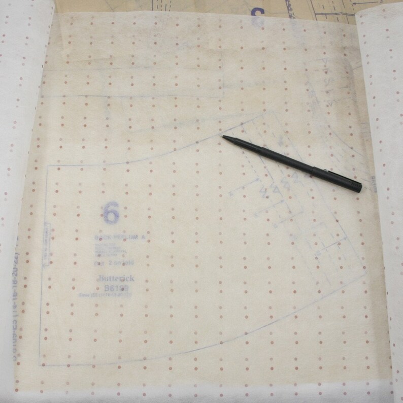 K&ouml;nnte beinhalten: Ein Schnittmuster mit der sichtbaren Zahl 6, zusammen mit der Marke "Butterick" und der Schnittnummer B6198. Ein schwarzer Stift liegt auf dem Muster. Das Muster befindet sich auf einem hellen, gepunkteten Papier.