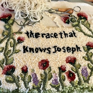 K&ouml;nnte beinhalten: Ein handgefertigter Teppich mit dem Text "the race that knows Joseph" in Schwarz. Der Teppich hat einen floralen Rand mit roten und lila Blumen und gr&uuml;nen Bl&auml;ttern. Eine Schere und Garn liegen obenauf.