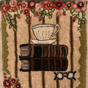 Peut inclure: Tapis fait à la main représentant une tasse et une soucoupe sur deux livres empilés. Le fond présente des rayures verticales, avec des accents floraux rouges, roses et verts. Une paire de petites lunettes est en bas.