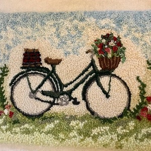 May include: Hand-tufted rug featuring a dark green bicycle with a basket of flowers and a basket on the back. The bicycle is set against a backdrop of a light blue sky and a field of flowers. The rug is rectangular.
