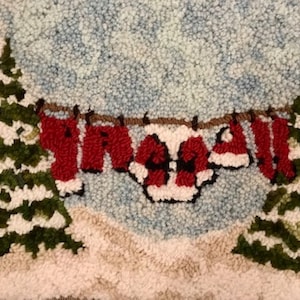 May include: A handmade Christmas-themed rug depicting a winter scene. Two green and white snow-covered fir trees frame a washing line with red Santa Claus clothing. The background is light blue, and the ground is white.