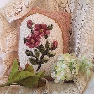 May include: A decorative pillow with a floral design. The pillow features a white background with a textured, embroidered floral pattern in shades of pink and green. The pillow is surrounded by lace fabric.