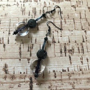 May include: A pair of dangle earrings featuring black lava rock beads, clear glass beads, and black metal wire. The earrings have a simple design and are ideal for everyday wear.