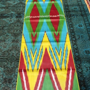 May include: A colorful fabric with a repeating pattern of red, yellow, green, and blue. The pattern is a traditional ikat design, which is a type of textile weaving.
