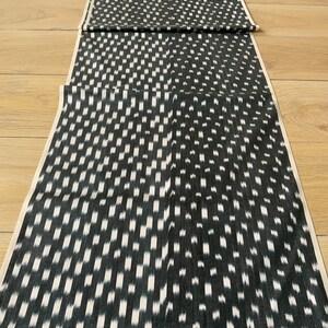 Könnte beinhalten: Schwarz-weißer Ikat-Stoff mit geometrischem Muster. Der Stoff ist dreifach gefaltet und auf einem Holzboden ausgelegt.