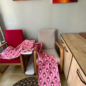 May include: Two chairs with pink and white patterned fabric draped over them. The chairs are in a room with a wooden cabinet and a rug on the floor.
