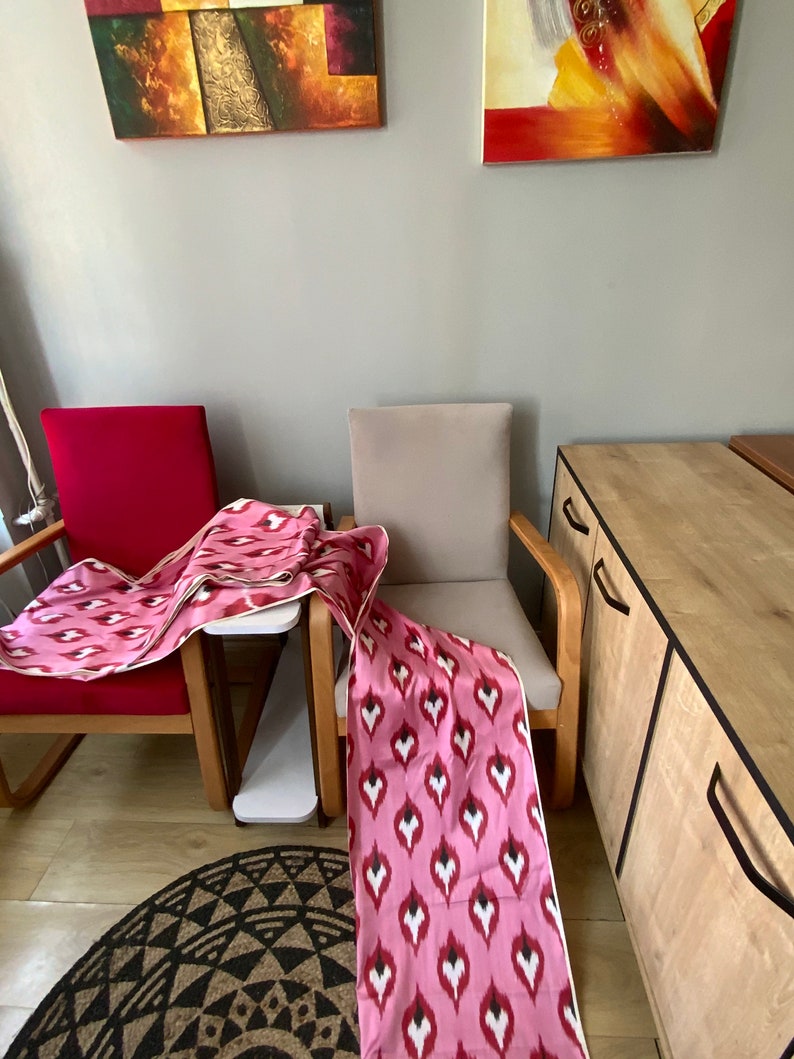 May include: Two chairs with pink and white patterned fabric draped over them. The chairs are in a room with a wooden cabinet and a rug on the floor.