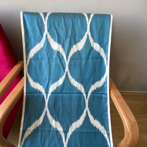 Könnte beinhalten: Ein blauer Stoff mit einem weißen geometrischen Muster. Der Stoff ist über einen Holzstuhl gelegt.