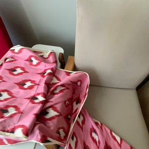 May include: A pink and white patterned fabric with a black and white ikat design. The fabric is folded and draped over a white surface and a chair.