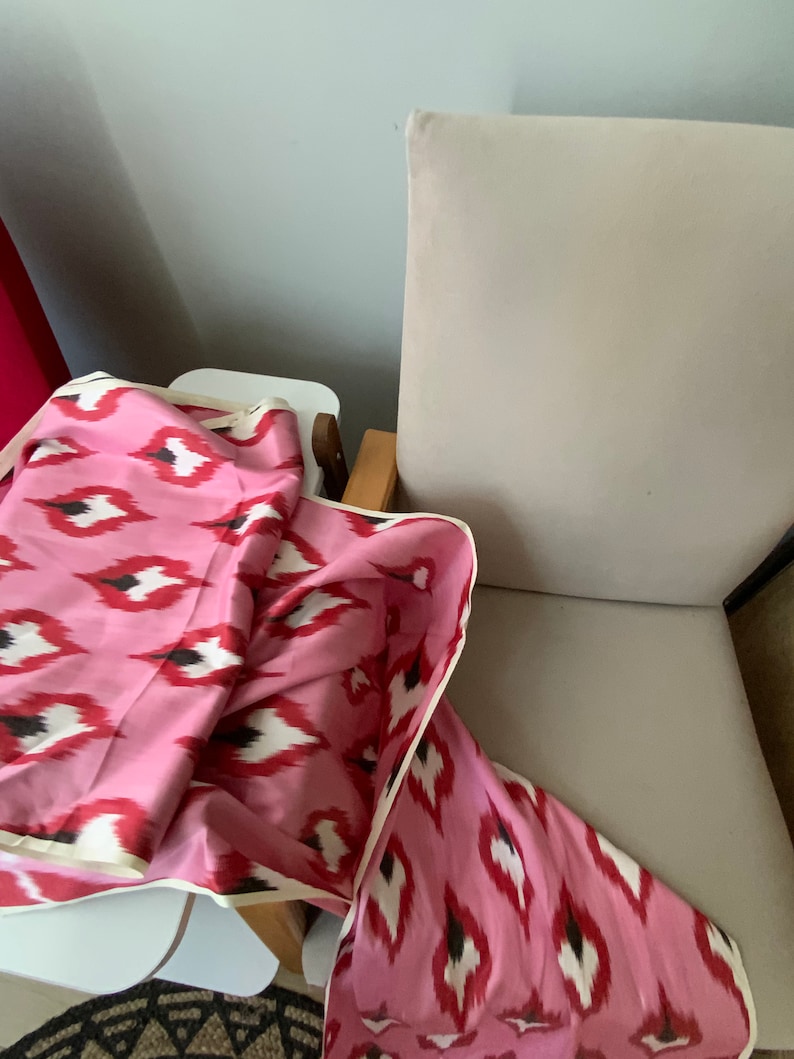 May include: A pink and white patterned fabric with a black and white ikat design. The fabric is folded and draped over a white surface and a chair.
