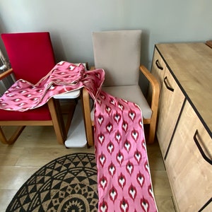 May include: Two chairs with pink and white patterned fabric draped over them. The chairs are in a room with a wooden cabinet and a patterned rug.