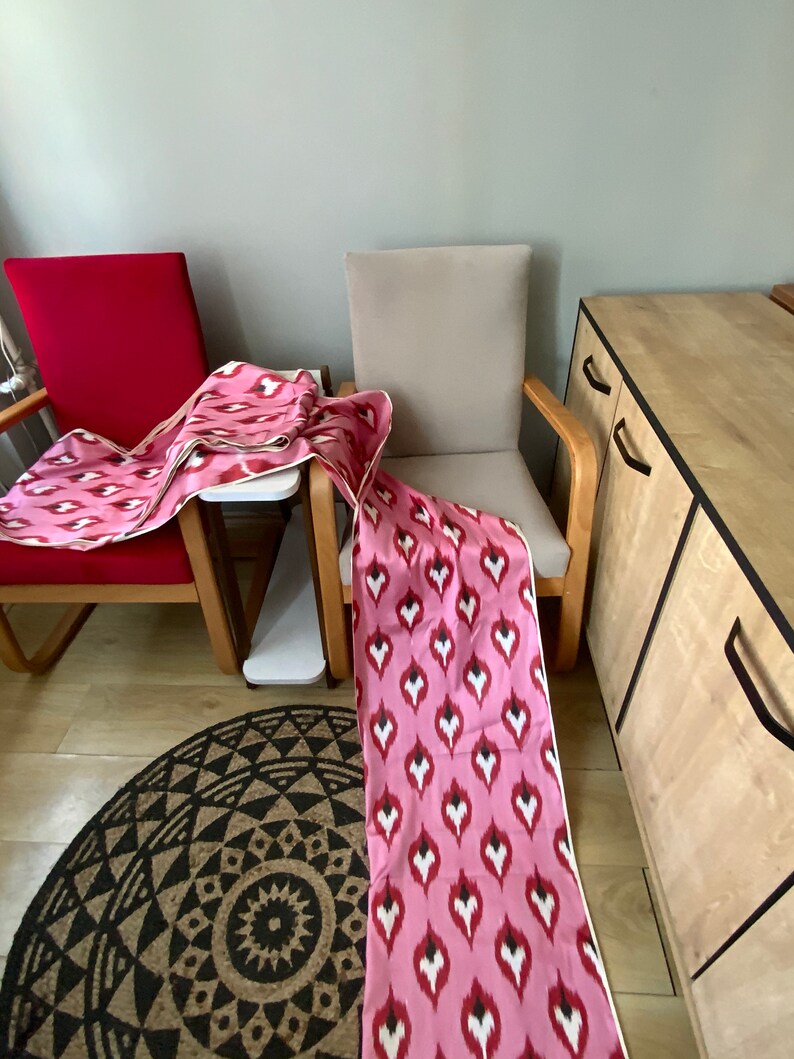 May include: Two chairs with pink and white patterned fabric draped over them. The chairs are in a room with a wooden cabinet and a patterned rug.