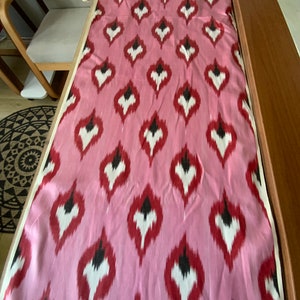 May include: Pink fabric with a repeating pattern of white, red, and black teardrop shapes.